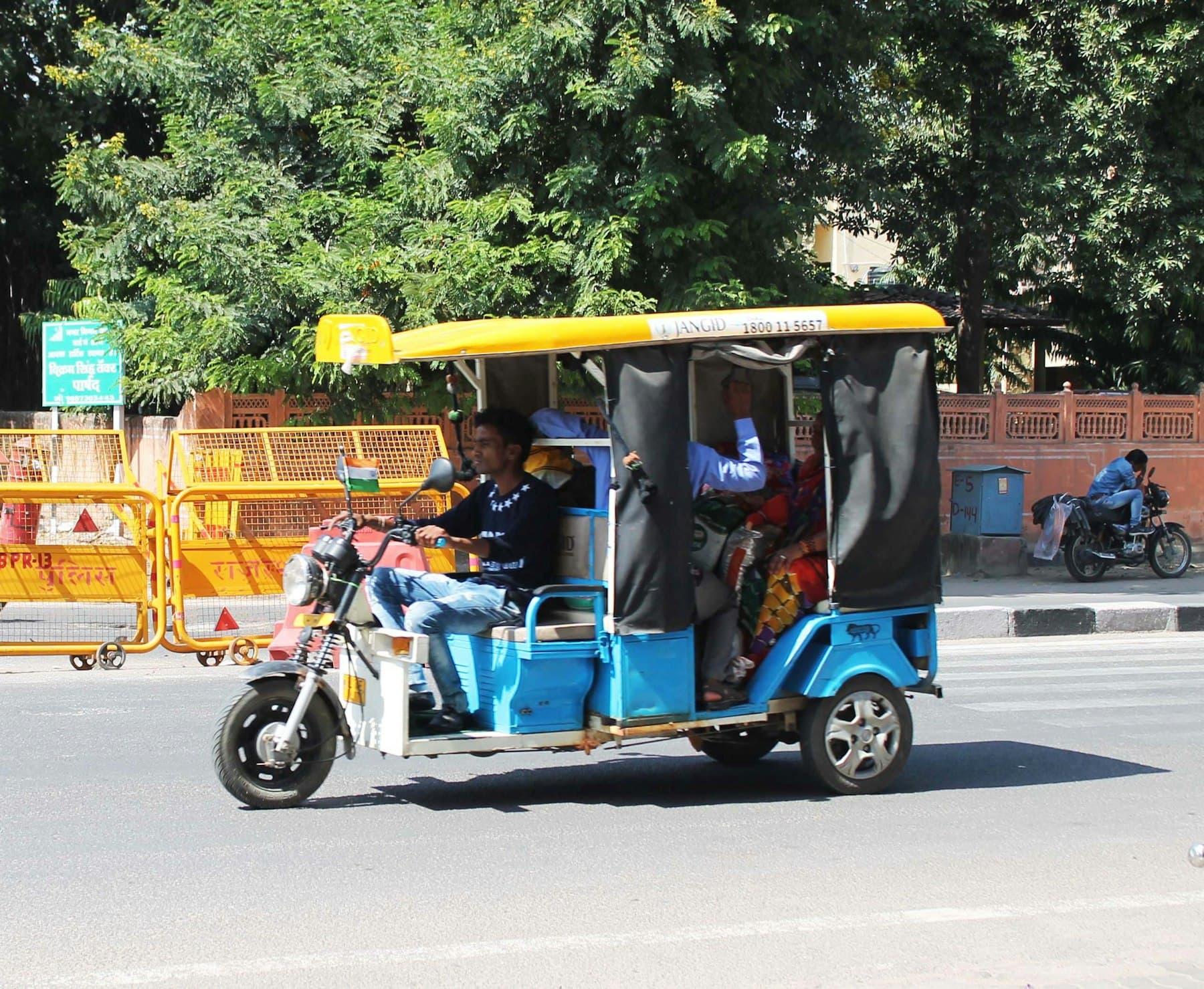 A battery e-rickshaw with a blue body and yellow canopy on a Delhi road