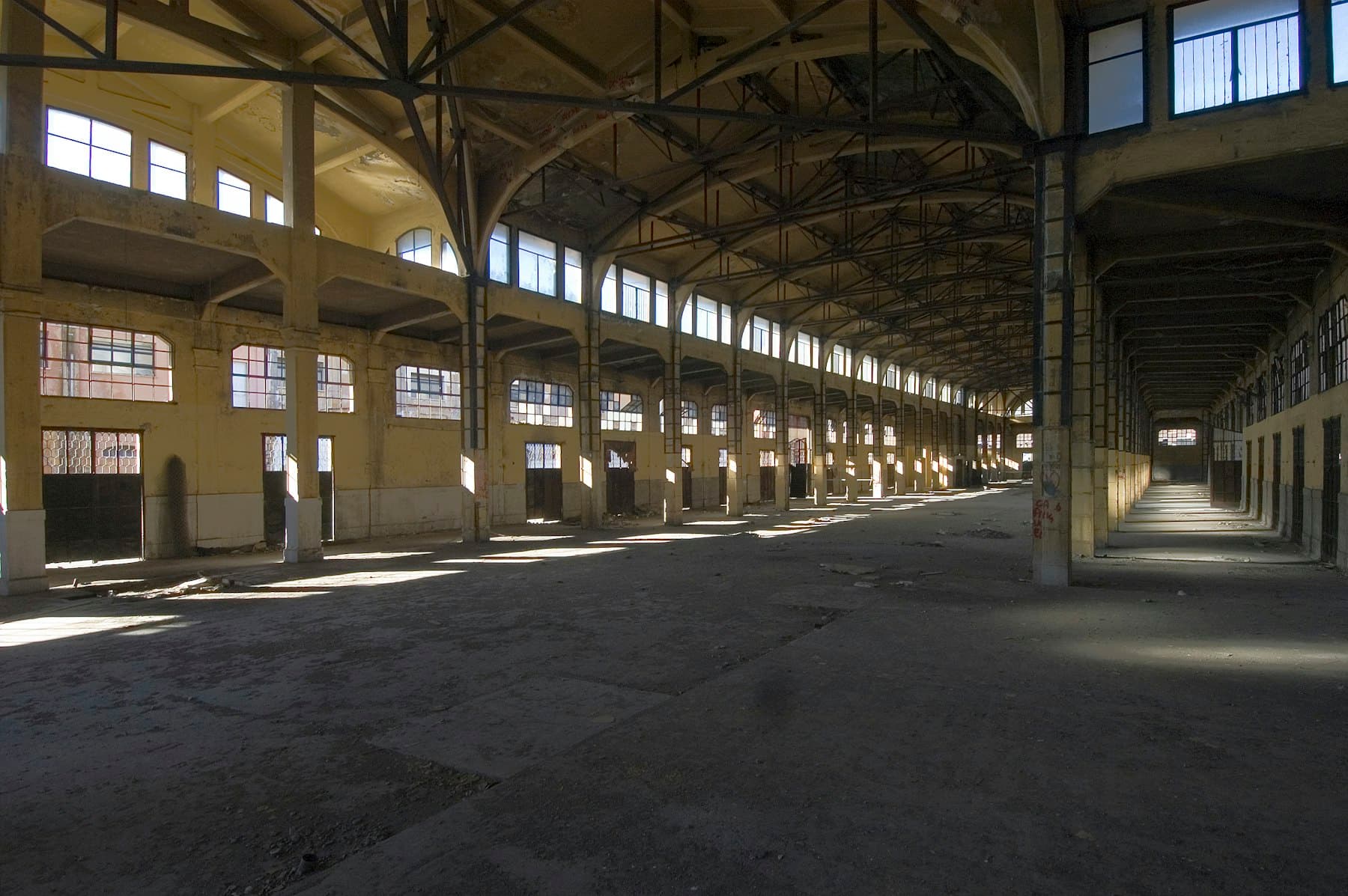 A vast industrial hall standing empty, lit by sunlight from high windows